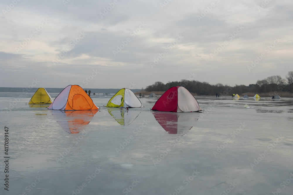 Winter fishing on the lake. Colorful tents for warm fishing in cold weather. Wallpaper. Selective focus.
