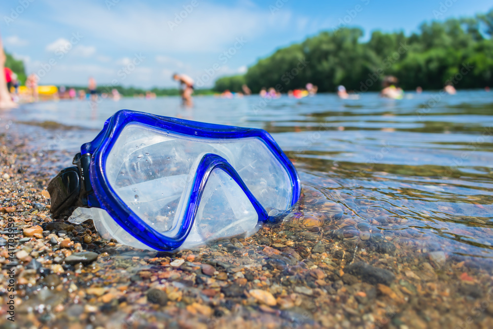 A swimming mask lies on a public beach near the water against the background of vacationing people