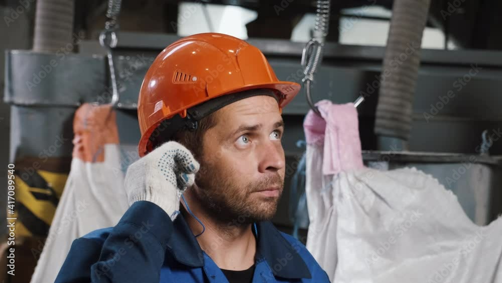 Portrait of worker in metallurgy factory, he wears helmet and ear plugs
