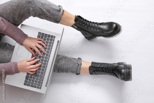 The woman uses a laptop on a white background. Female legs in jeans and boots. Online work. Top view