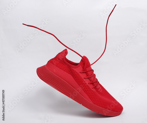 Red sports shoe with flying laces on white background