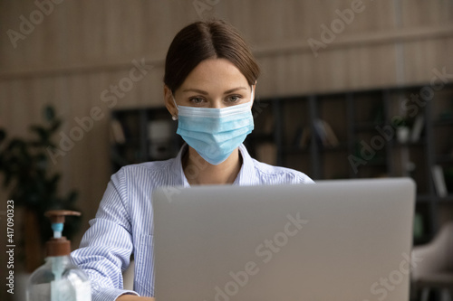 Focused businesswoman in facemask look at laptop screen work online during coronavirus pandemics quarantine. Concentrated Caucasian female employee in facial mask use computer. Covid-19 concept.