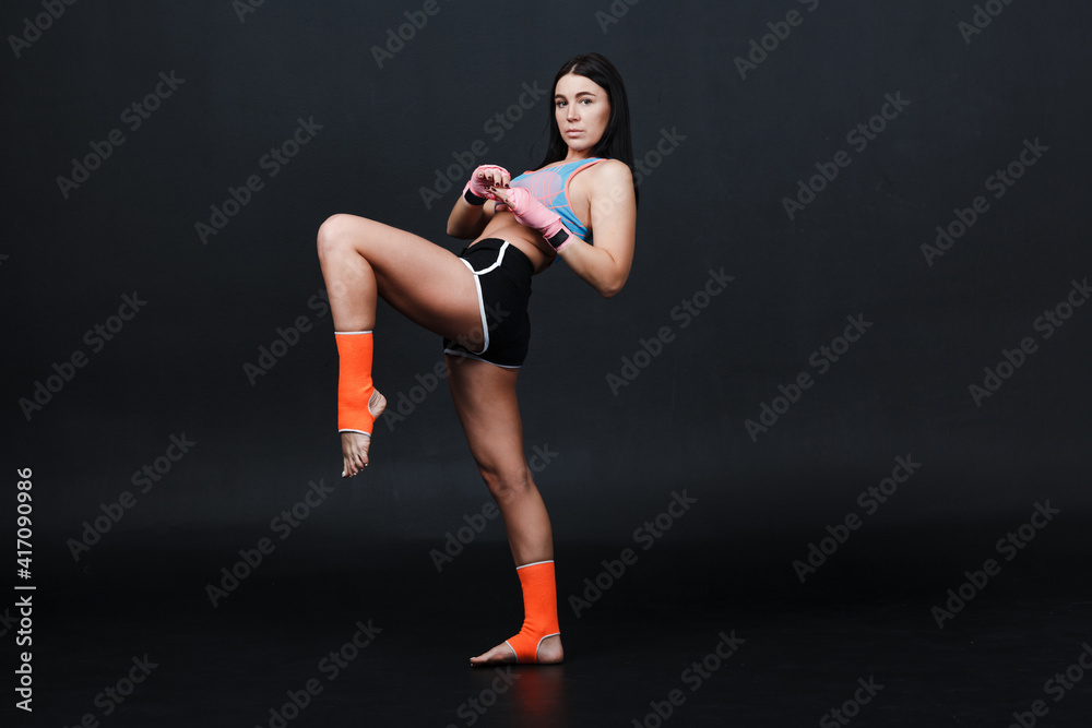 Sporty muay thai woman boxer posing in training studio at black background.