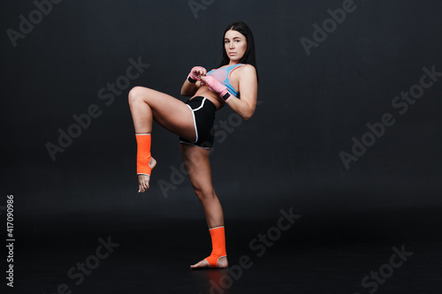 Sporty muay thai woman boxer posing in training studio at black background.