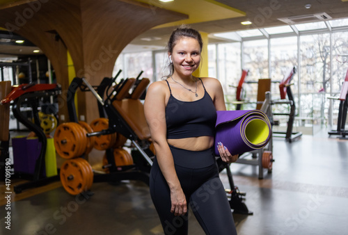 Young attractive fit woman with mat in her hands in gym