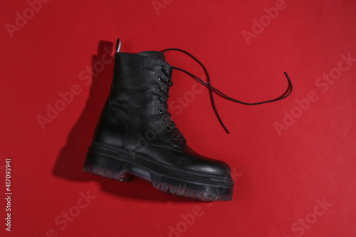 Stylish female leather boot with high soles on a red background with a shadow