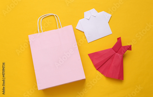 Shopping bag with origami dress and shirt on a yellow background. Shopping concept © splitov27