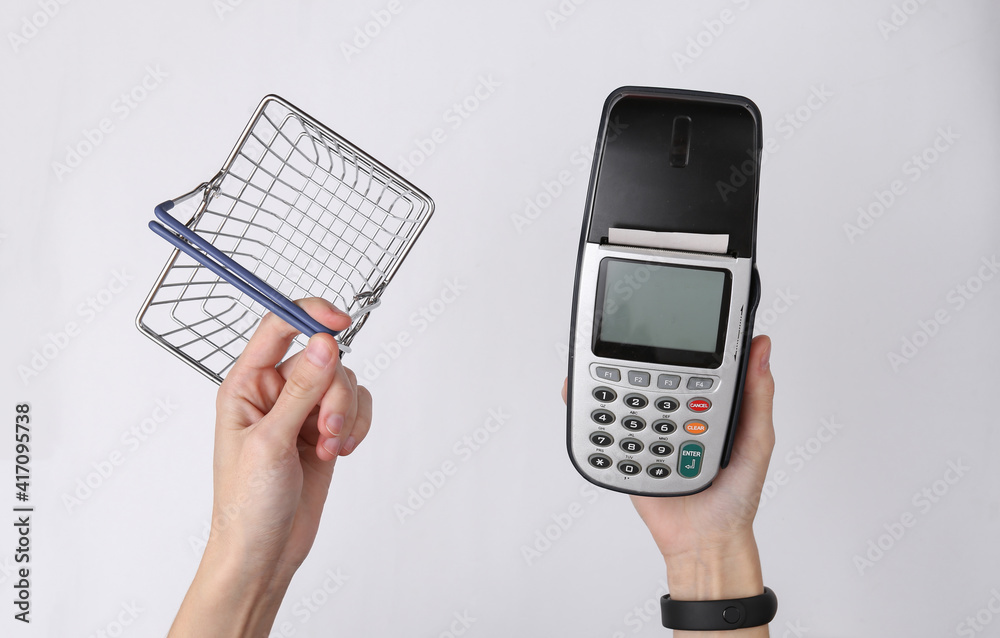 Hand holds payment terminal and supermarket basket on white background. Payment for purchases Hand holds payment terminal and supermarket basket on white background. Payment for purchases