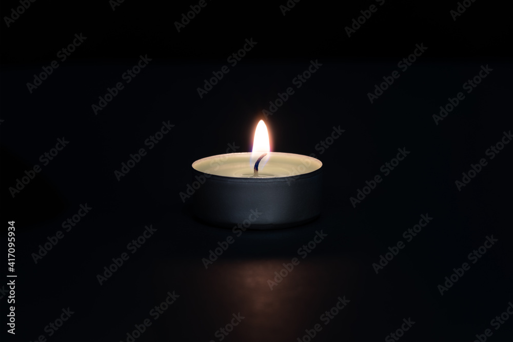 A burning candle on a dark background with a flare in the foreground. A burning candle on a dark background with a flare in the foreground.