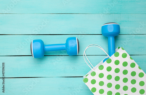 Paper polka dots shopping bag with dumbbells on blue wooden background. Sport shopping. Top view
