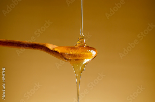 Spoon with a pouring drop of golden honey on yellow background
