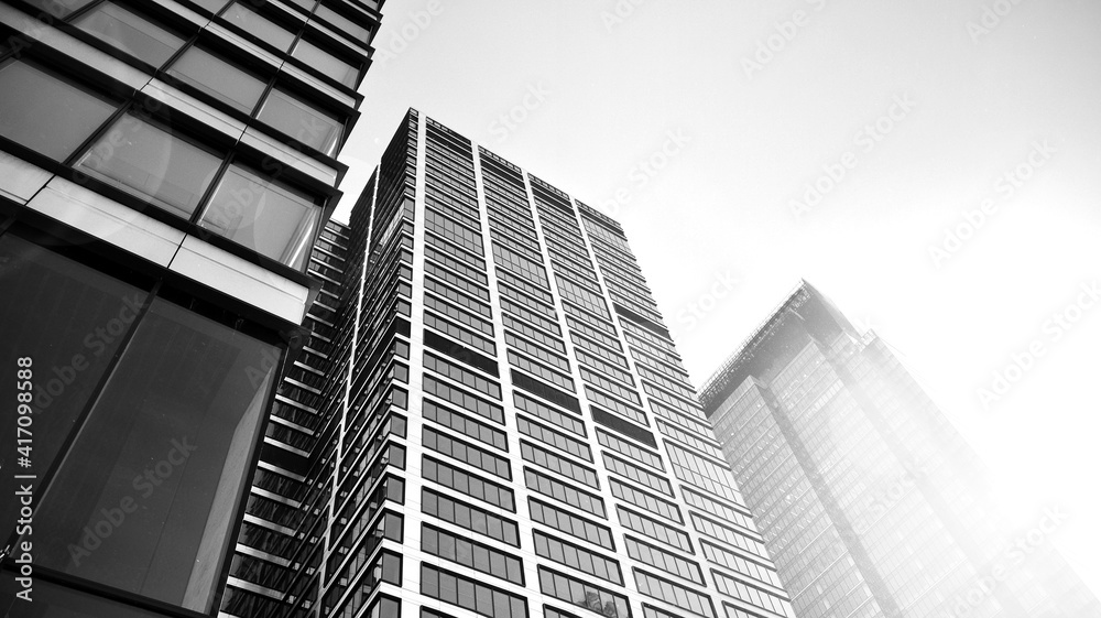 Bottom view of modern skyscrapers in business district against sky. Looking up at business buildings in downtown. Rising sun on the horizon. Black and white.
