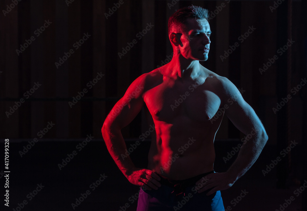 Athletic handsome man athlete with naked torso in red blue gradient neon light on black background
