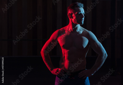 Athletic handsome man athlete with naked torso in red blue gradient neon light on black background