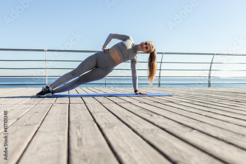 Young slim fit Caucasian woman practicing side plank on the beach. Healthy lifestyle