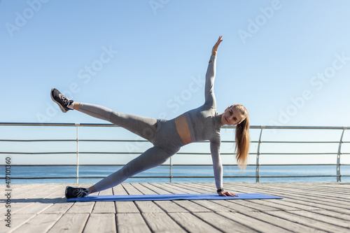 Fototapeta Naklejka Na Ścianę i Meble -  Young slim fit Caucasian woman practicing side plank on the beach. Healthy lifestyle