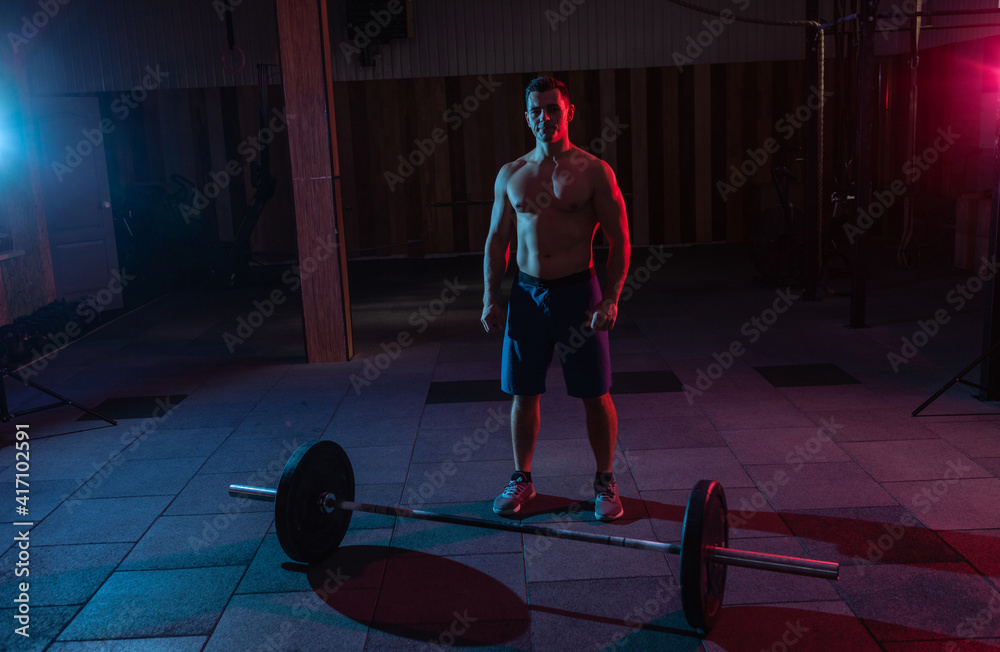 Fototapeta premium Muscular powerful man and barbell in red-blue neon light in a cross-training gym