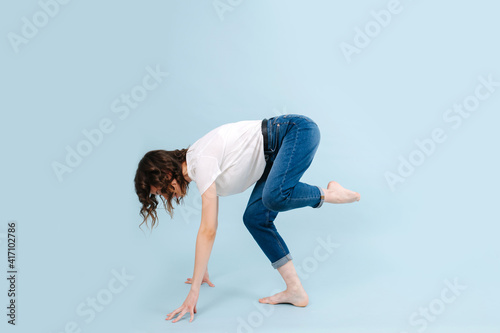 Contemporary dancer poses in front of blue studio background. She's standing on two hands and one leg, shifing her weigth forward. photo