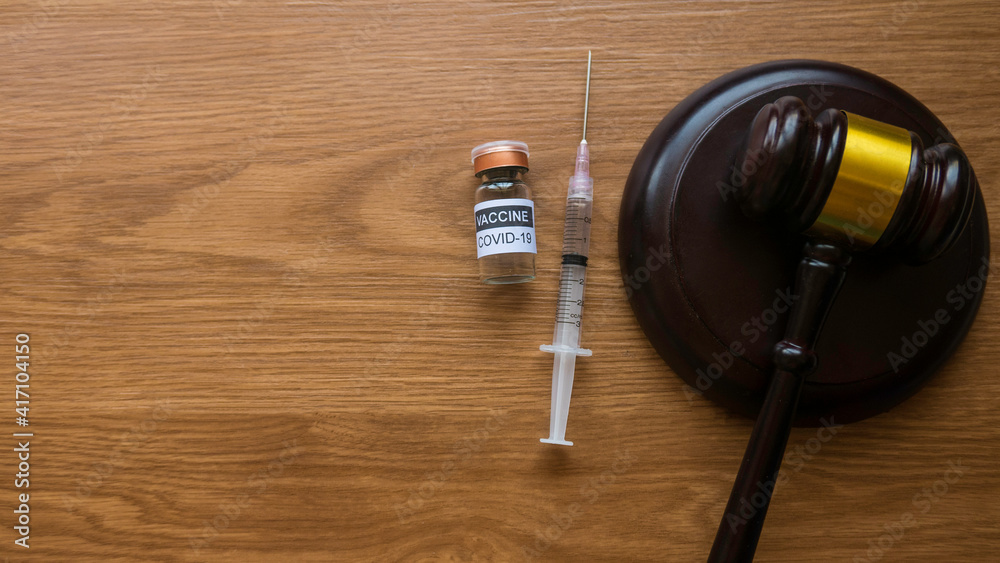 Law and vaccination concept. Top view of bottle of covid-19 vaccine, gavel and syringe on wooden background with copy space. Law and vaccination concept. Top view of bottle of covid-19 vaccine, gavel and syringe on wooden background with copy space.