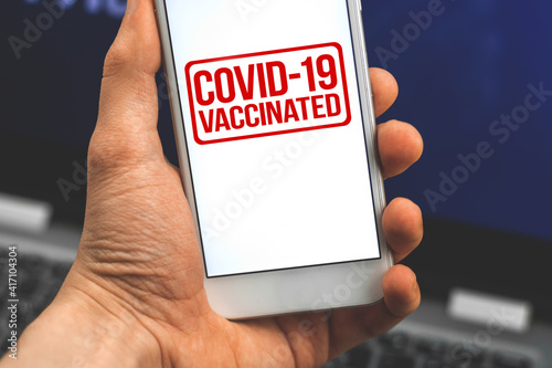 Digital vaccinate app, COVID-19 vaccinated label on a screen of smartphone in hand