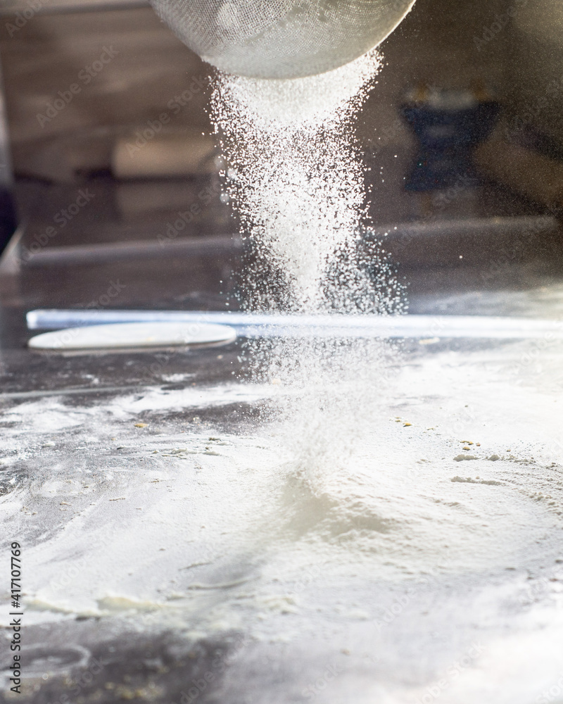 Obraz premium White flour is poured onto a metal table through a sieve. Sifting flour for dough