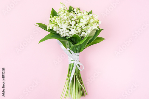 Spring lily of the valley flowers bouquet on pastel pink background. Flat lay. Top view. Wedding concept