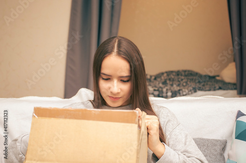 Delivery of parcels and orders from the online store. Girl opens a box at home