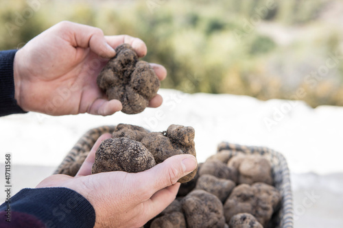 A caucasian man shows some black truffles from a basket.