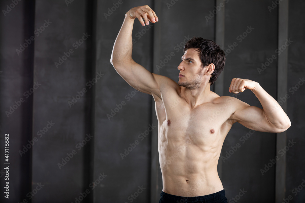 Beautiful young strong man posing on dark background.