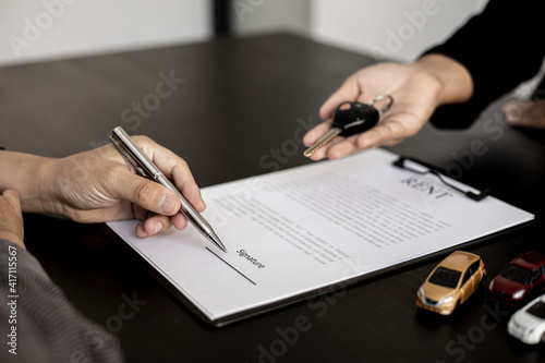 The renter is signing a car rental agreement with the car rental company. After discussing the details and charges with the employee, the employee hand over the car keys to the renter.
