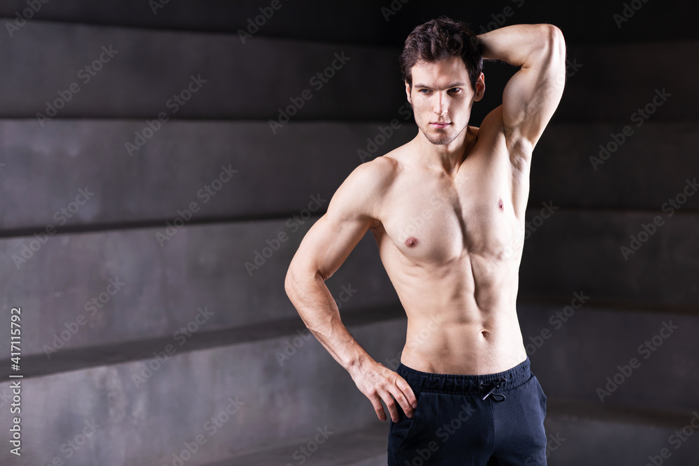 Handsome strong man posing over creative dark background.
