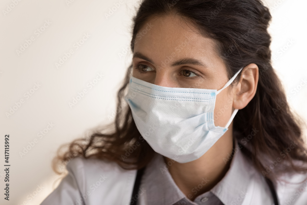 Close up thoughtful female doctor wearing medical protective face mask and uniform looking to aside, pensive therapist physician gp thinking about problem solution, planning or listening to patient