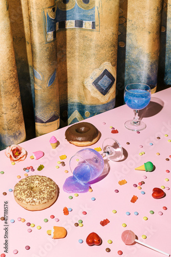 Minimal after party concept with small ice cream, pink creative drink in wine glasses, candies and lolly pop all over the pink table background and gold silk or saten curtain.