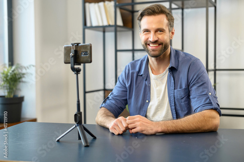 Blogging concept. Young bearded hipster male blogger vlogger streaming video online or recording tutorial for social media network, creating content for followers, smiling and looking at the camera