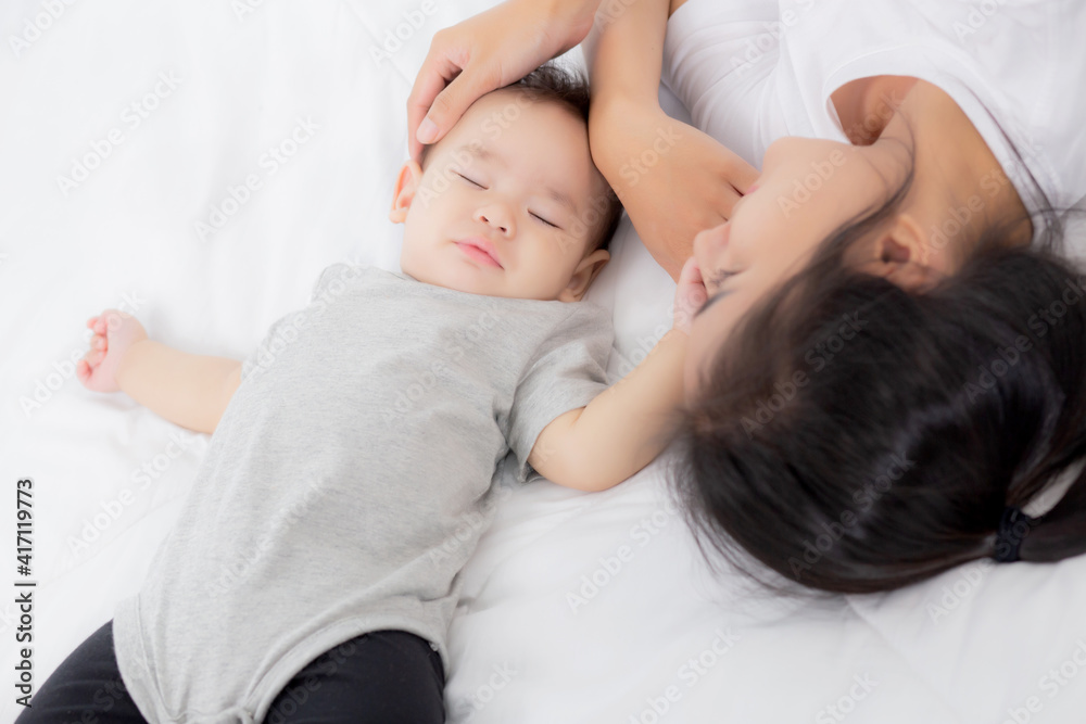 Young asian mother touch head of little baby girl with tender on bed in the bedroom, mom love newborn and care, woman with expression with child together, parent and daughter, family concept. Young asian mother touch head of little baby girl with tender on bed in the bedroom, mom love newborn and care, woman with expression with child together, parent and daughter, family concept.