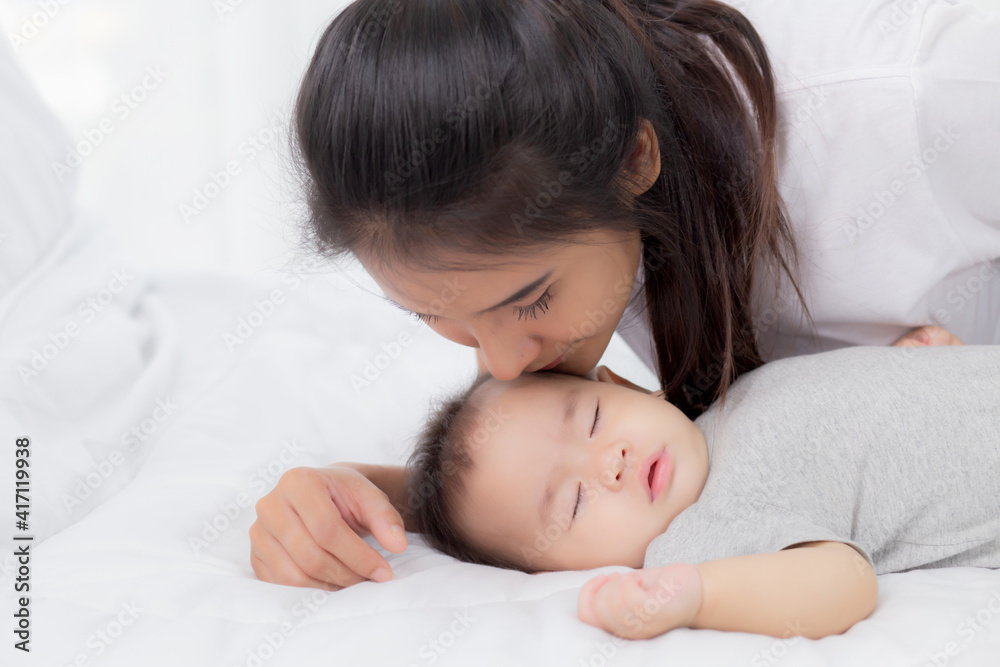 Young asian mother kiss cheek of little baby girl with tender on bed in the bedroom, mom love newborn and care, mother with expression with child together, parent and daughter, family concept. Young asian mother kiss cheek of little baby girl with tender on bed in the bedroom, mom love newborn and care, mother with expression with child together, parent and daughter, family concept.