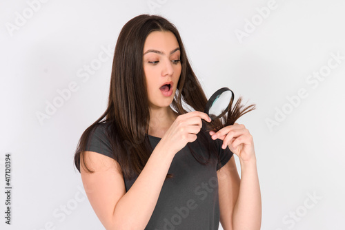 hair and head skin problem, beautiful girl surprised and unhappy with her dry and damaged hair ends , holding magnifier