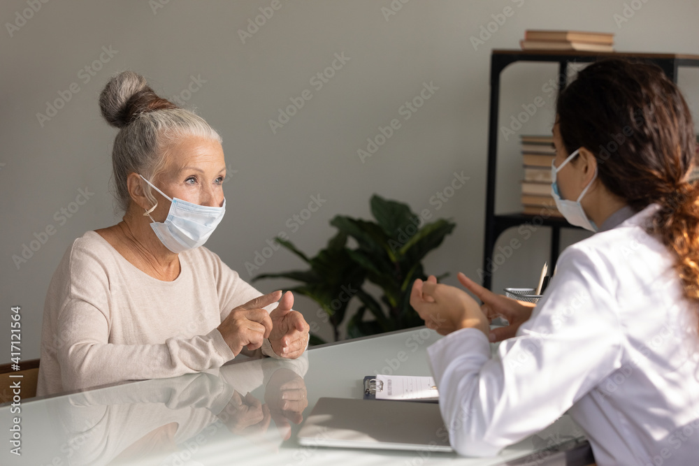 Close up mature woman wearing medical face mask listening to doctor during appointment in hospital office, female therapist practitioner consulting older patient about treatment, elderly healthcare Close up mature woman wearing medical face mask listening to doctor during appointment in hospital office, female therapist practitioner consulting older patient about treatment, elderly healthcare