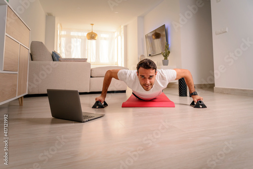 Young cheerful man doing push ups in room during quarantine