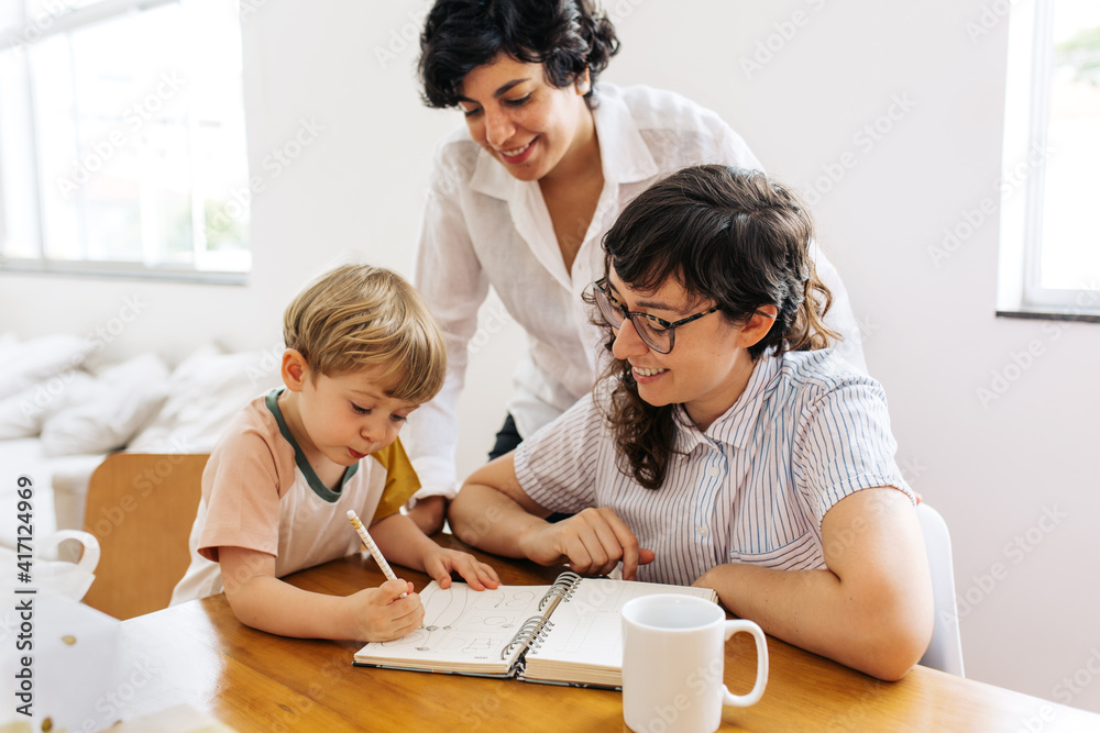 Female couple looking at their son scribbling in a book Female couple looking at their son scribbling in a book