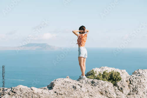 A young girl stands on the edge of a cliff and looks at the sea. © Alex Photo