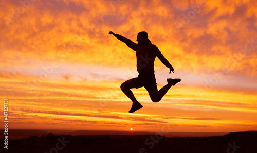 Silhouette of a happy man traveler with a raised hand in a jump on a sunset background. Success concept.