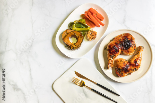 Roasted chicken leg with spice and vegetables sliced on dish, ready to served. Top view and copy space on white table background.