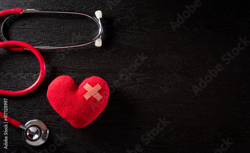 Top view of red heart with doctor physician's stethoscope on dark stone background. Hospital life insurance concept, World health day concept.