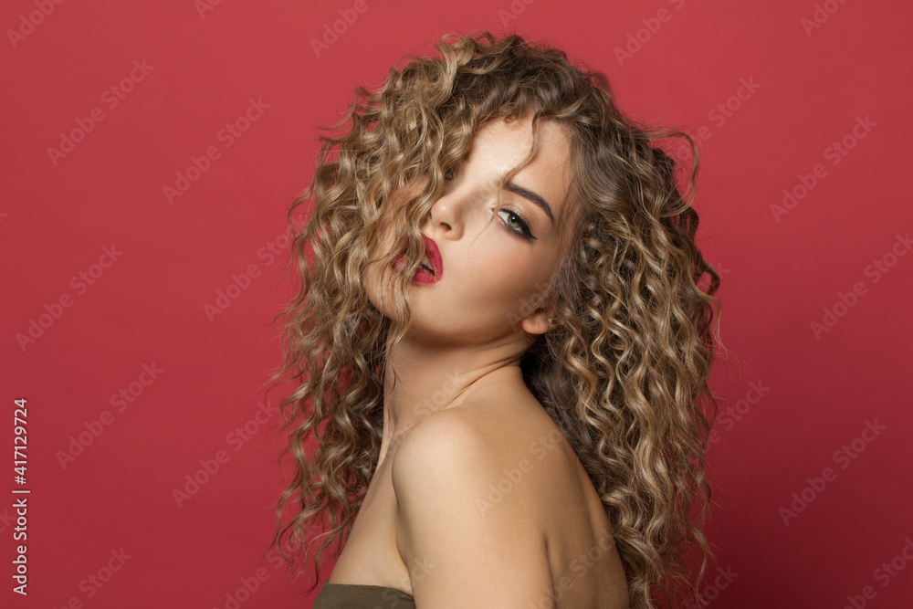 Fototapeta premium Cheerful beauty. Cute woman with curly hair on red background