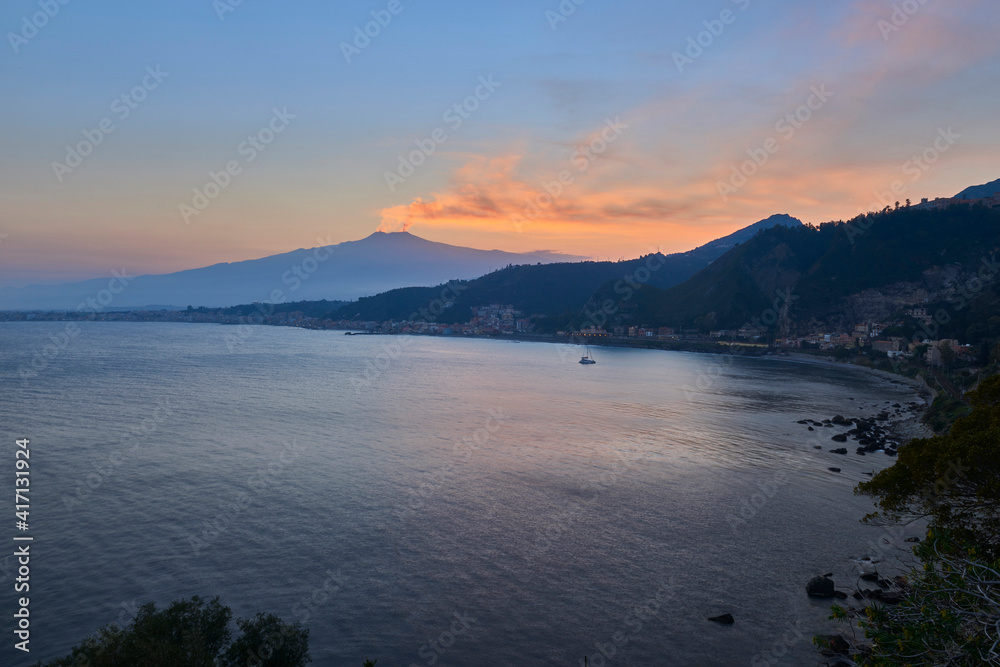sunset on the bay of Taormina With the smoking Etna Volcano, which dominates the scene, and the sky is colored