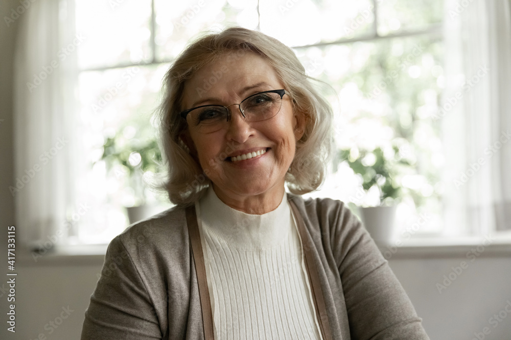 Photo portrait of happy elder OAP 60s woman wearing glasses, looking at camera with toothy smile. Head shot of mature female pensioner enjoying good health, safe and wellbeing. Videocall screen view