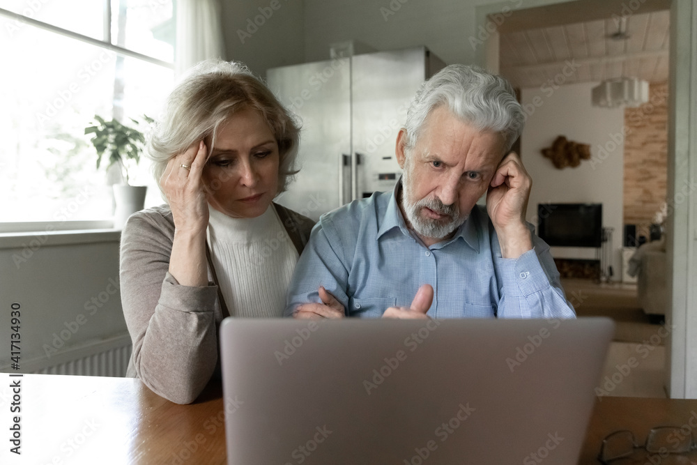 Upset 60s senior couple getting shocking bad news, using laptop together at home, reading email message or talking via video call. Frustrated elder retired husband and wife looking at computer screen Upset 60s senior couple getting shocking bad news, using laptop together at home, reading email message or talking via video call. Frustrated elder retired husband and wife looking at computer screen