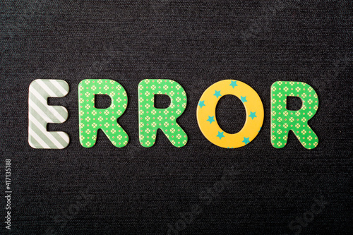 Card with Error word made from mixed vivid colored wooden letters on a textured dark black textile material that can be used as a message.