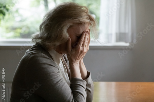 Depressed elder OAP 60s woman goes through crisis  loss  grief  dementia. Unhappy middle aged female pensioner covers face with hands in despair after receiving bad shocking news about health problem